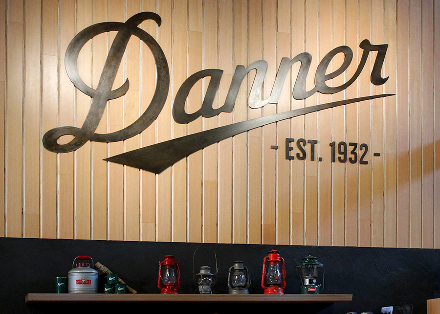 A large Danner logo in laser-cut metal set on hardwood planks visually anchored using vintage camping gear